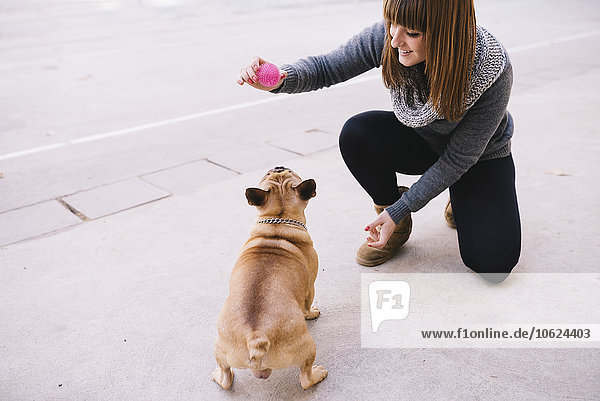 Junge Frau spielt mit ihrer französischen Bulldogge auf dem Bürgersteig