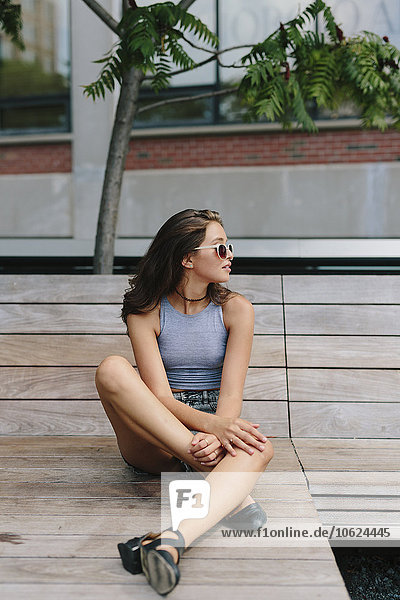Brunette young woman wearing sunglasses relaxing on bench