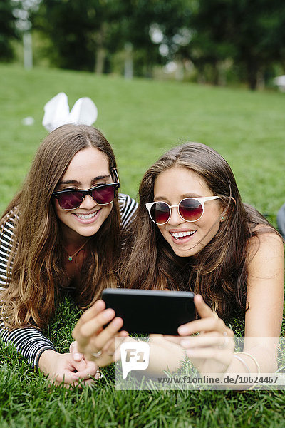 Zwei glückliche Freunde in einem Park mit Blick auf das Handy