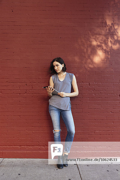 Porträt einer Frau mit digitalem Tablett an der roten Ziegelwand lehnend