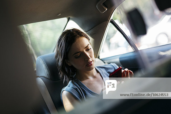 Porträt einer jungen Frau  die mit ihrem Smartphone in einem Taxi sitzt.