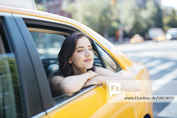 USA  New York City  Porträt einer jungen Frau  die sich aus dem Fenster eines gelben Taxis lehnt.