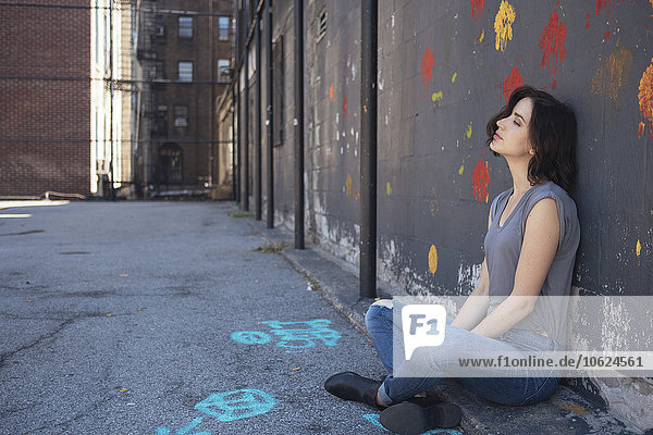 USA  New York City  junge Frau auf dem Boden sitzend an einer Wand lehnend