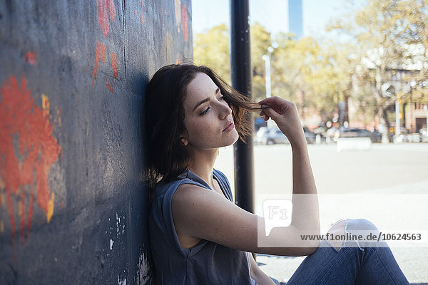 USA  New York City  träumende junge Frau auf dem Boden sitzend an einer Wand lehnend