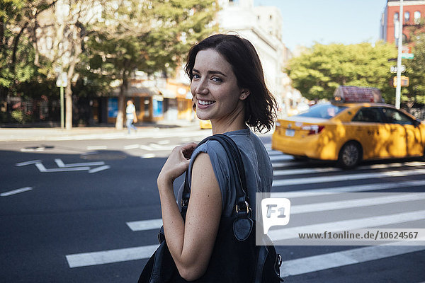 USA  New York City  Manhattan  Portrait einer lächelnden jungen Frau beim Überqueren einer Straße