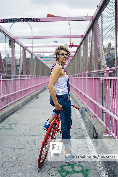 USA  New York City  Williamsburg  lächelnde Frau mit rotem Rennrad auf der Williamsburg Bridge