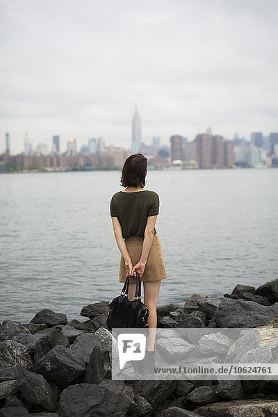 USA  New York City  back view of young woman looking to Manhattan skyline from Williamsburg bank