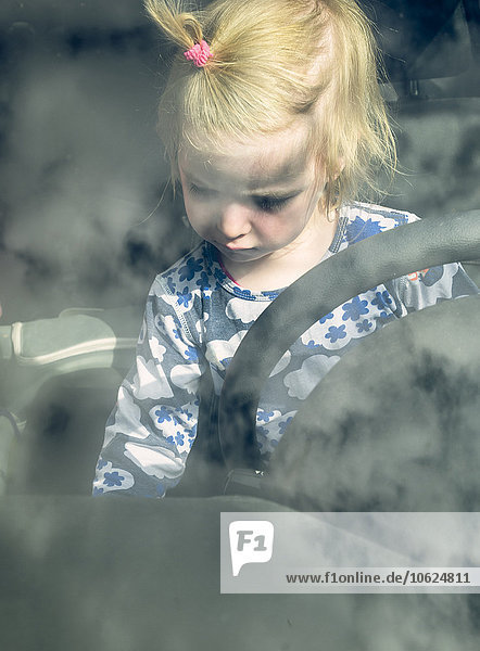 Blondes Kleinkind sitzt hinter dem Lenkrad in einem Auto