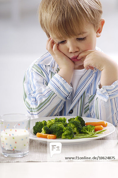 Porträt des kleinen blonden Jungen mit Blick auf den Teller mit Gemüse