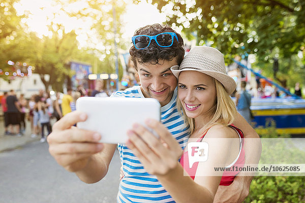 Glückliches Paar auf der Kirmes mit Smartphone Selfie
