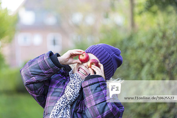 Kleines Mädchen  das seine Augen mit zwei Äpfeln bedeckt.