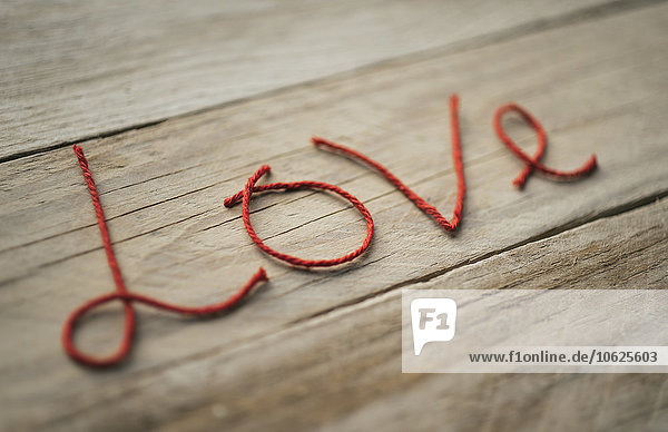 Das Wort'Liebe' aus roten Fäden auf Holz