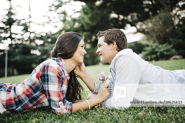 Verliebtes junges Paar liegt von Angesicht zu Angesicht auf einer Wiese im Park