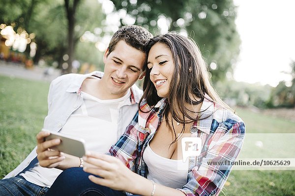 Porträt eines jungen verliebten Paares  das etwas auf einem Smartphone im Park sieht.