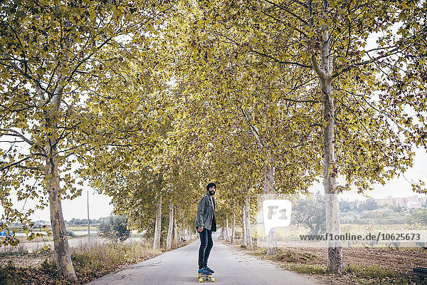 Spain  Tarragona  young man with longboard on autumnal country road