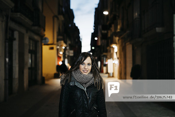 Spanien  Reus  Porträt einer lächelnden jungen Frau  die abends in einer Gasse steht.
