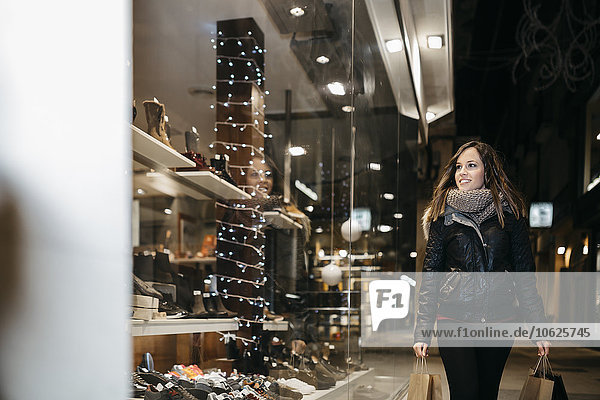 Spain  Reus  smiling young woman looking at window display in the evening