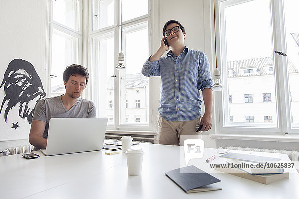 Zwei kreative Geschäftsleute mit Laptop und Handy in einem modernen Büro