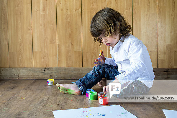 Little boy sitting on wooden floor using finger colours