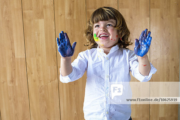 Portrait eines lächelnden kleinen Jungen  der seine Handflächen voller blauer Fingerfarbe zeigt.