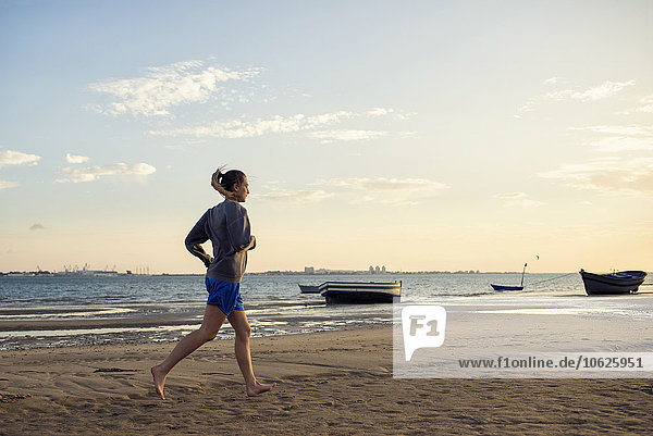 Spanien  Puerto Real  Frau beim Joggen am Strand bei Abenddämmerung
