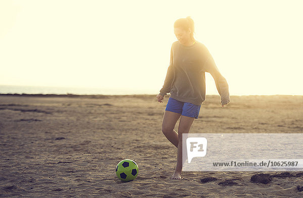 Spanien  Junge Frau spielt Fußball am Strand