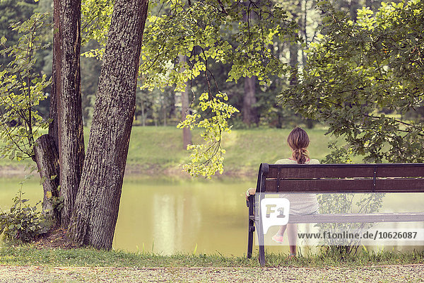 Russland  Sankt Petersburg  Rückansicht einer Frau  die auf einer Bank sitzt und das Wasser im Schuwalowskij-Park betrachtet.