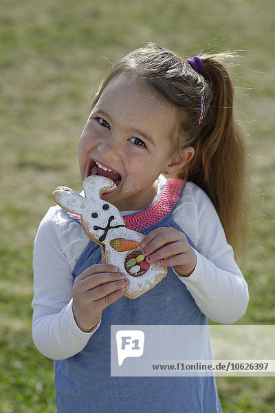 Portrait of smiling little girl biting off pastry formed like an Eastern Bunny