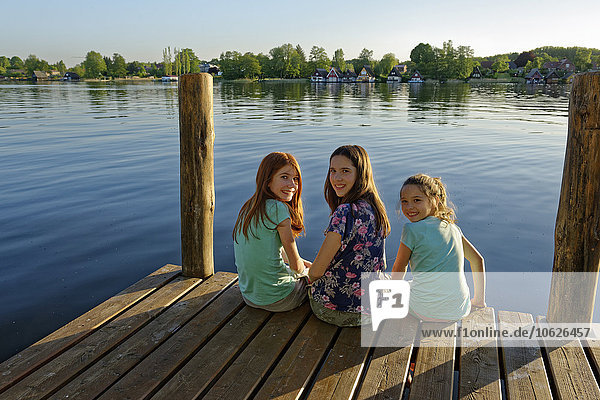 Germany  Mirow  three girls sitting on a jetty at Lake Mirow