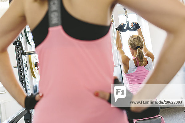 Woman watching athlete doing lat pulldowns in gym