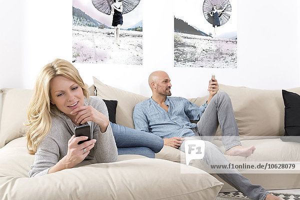 Reife Paare  die auf dem Sofa sitzen und ihre Smartphones benutzen.