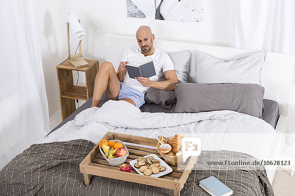Erwachsener Mann mit Büchern und Frühstück im Bett