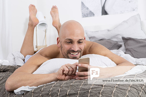 Erwachsener Mann mit auf dem Bett liegendem Smartphone