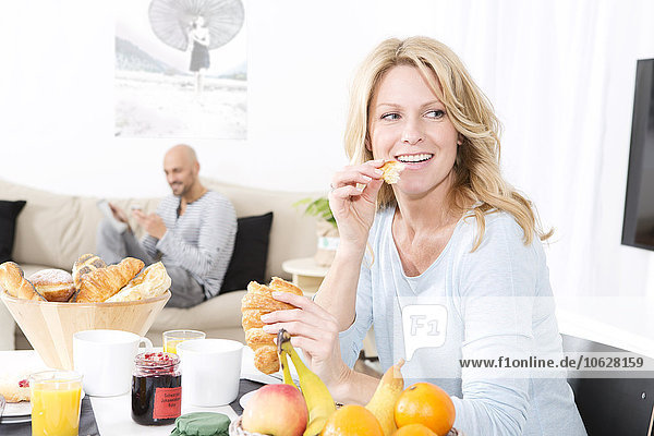 Mature woman having breakfast while man is talking at the phone