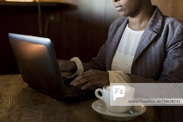 Junge Frau sitzt in einem Café und arbeitet mit einem Laptop.