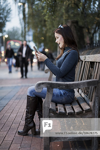 Glückliche Frau schaut auf Smartphone auf einer Bank