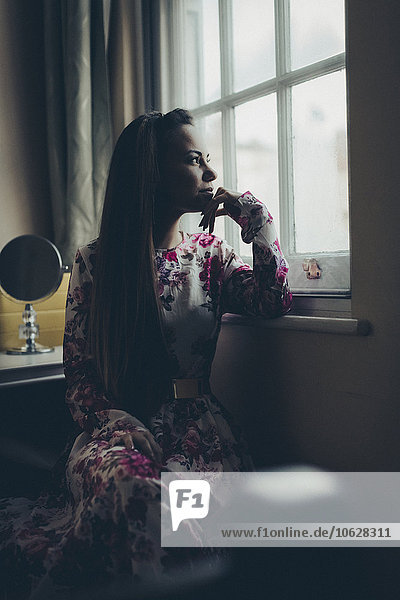 Young woman in floral dress looking out of window