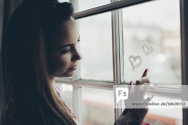 Junge Frau zeichnet Herzen auf beschlagener Fensterscheibe