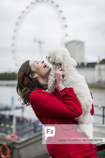 UK  London  glückliche junge Frau mit Hund auf den Armen und London Eye im Hintergrund
