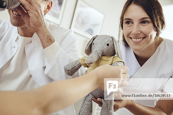 Krankenschwester  die das Kind mit Spielzeug ablenkt  während der Arzt mit einem Operationsmikroskop die Ohren untersucht.