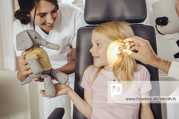 Krankenschwester  die das Kind mit Spielzeug ablenkt  während der Arzt mit einem Operationsmikroskop die Ohren untersucht.