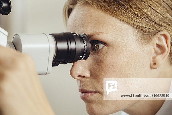 Profile of female doctor looking through surgical microscope