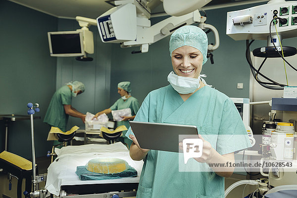 Lächelnde Chirurgin im Operationssaal mit Blick auf das digitale Tablett