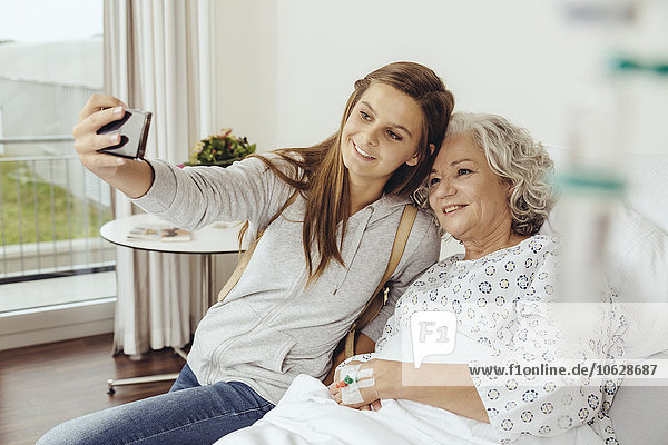 Granddaughter visiting grandmother in hospital  taking selfie with smart phone