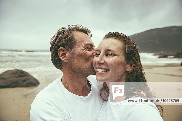 Brasilien  Florianopolis  Mann küsst Frau am Strand an einem regnerischen Tag