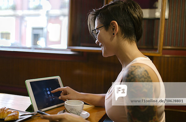 Tätowierte junge Frau sitzend in einem Coffee-Shop mit digitaler Tablette