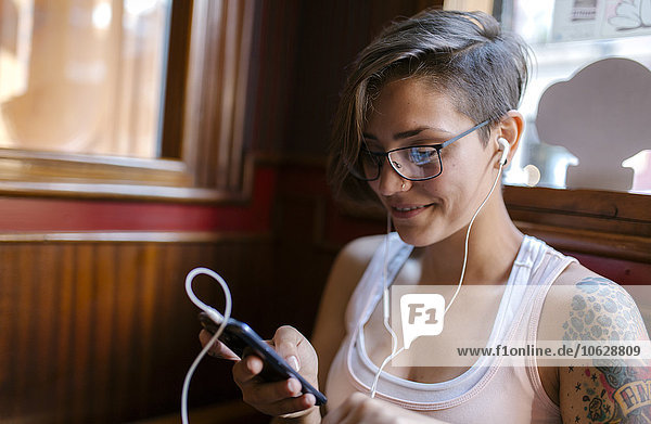 Tattooed young woman listening music with earphones