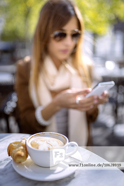 Spanien  Gijon  Cup of cappucino  junge Frau im Hintergrund mit Smartphone