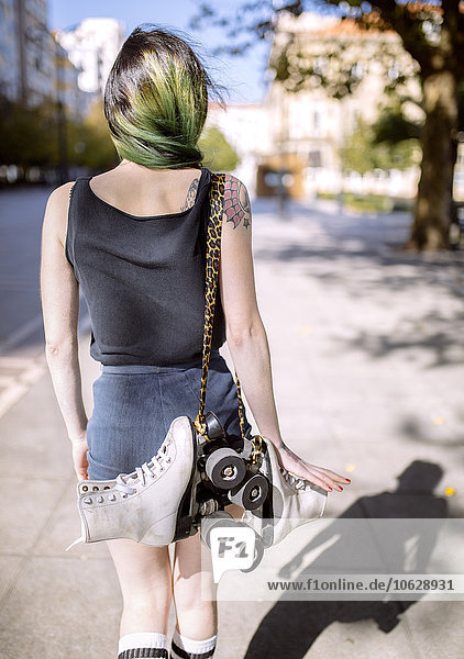 Spanien  Gijon  Rückansicht einer jungen Frau mit grün gefärbten Haaren  die Inline-Skates über der Schulter trägt.