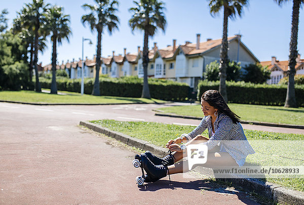 Spanien  Gijon  Teenagermädchen auf dem Bordstein sitzend  ihre Rollschuhe bindend